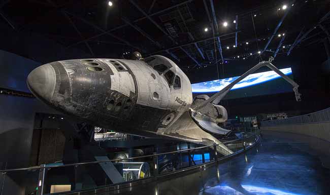 A life-sized space shuttle appears to be banking into a turn at a museum exhibit.